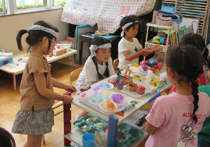 5歳児が工作でつくったかき氷やアイスのご馳走をお客さんにすすめている様子