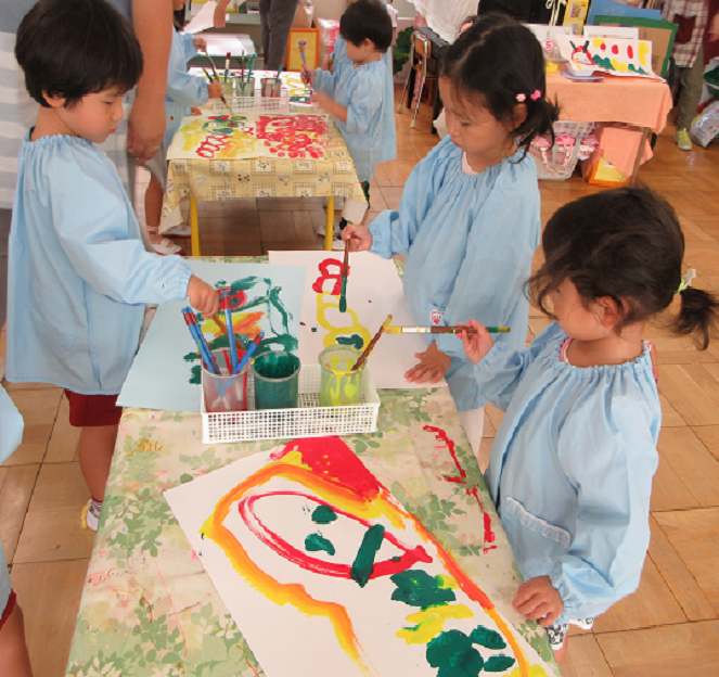 3歳児が黄色と緑色と赤色の絵の具を使って青虫の絵をかいているところ