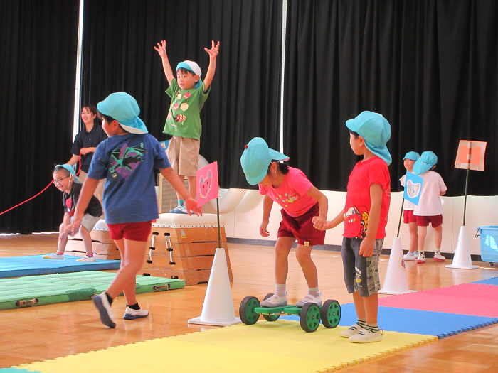 5歳児が遊戯室でペダルローラーやジャンプなどの運動遊びを楽しんでいるところ
