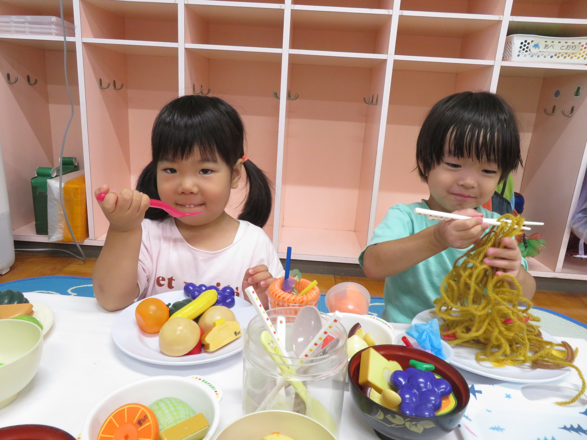 男の子と女の子がおもちゃのごちそうや毛糸のおそばを食べて遊んでいる