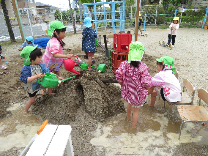 4歳児の子ども4人が砂場の山に樋を刺し、水を流して遊んでいる姿