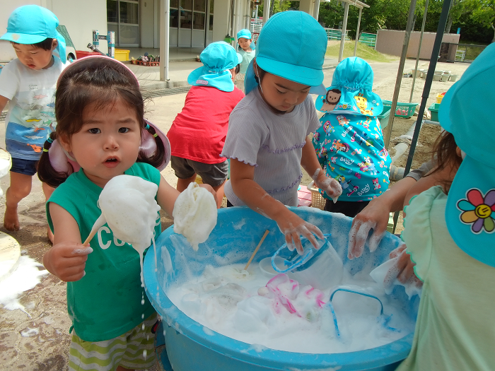 2歳児がたらいに入った石鹸の泡で遊んでいる