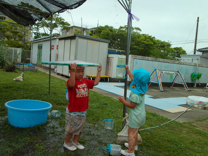 ビニールを貼ったフラフープをもって、シャワーの水から身を守っている3歳児