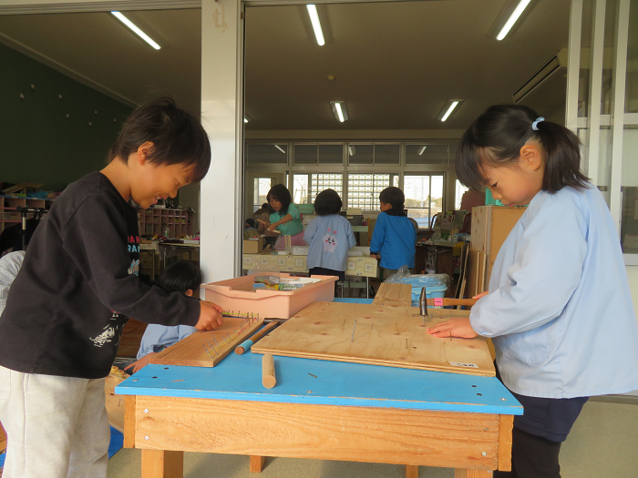 5歳児が二人でにこにこしながら木の板にくぎを打ち付けている
