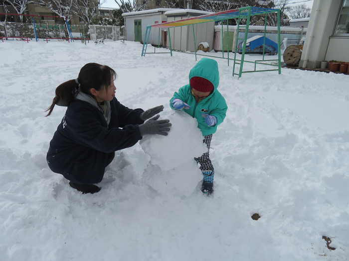 2歳児と保護者が一緒に雪だるまを作っている
