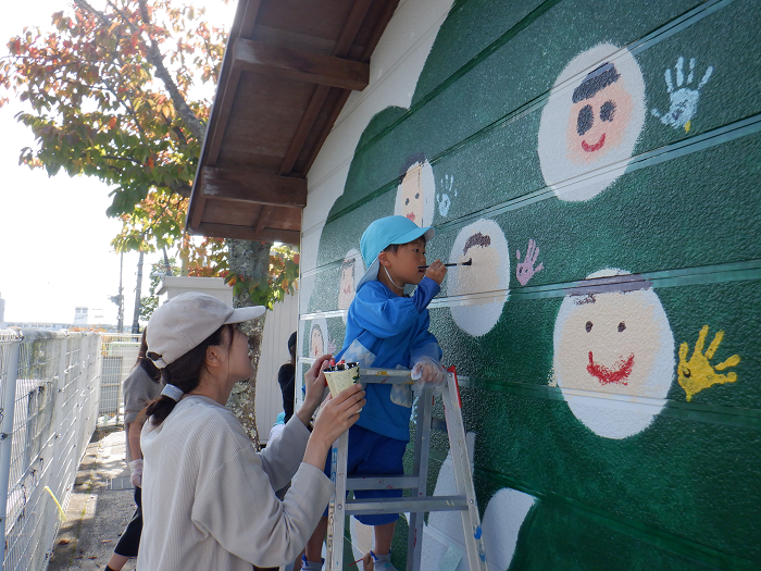 脚立にのって、おうちの方と壁に絵をかいている5歳児