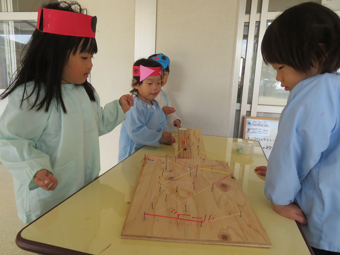 5歳児が木にくぎを打ち付けて作ったビー玉転がしを3歳児がさせてもらって喜んでいる
