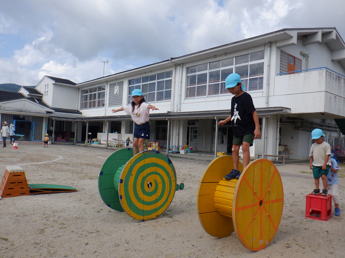 大きな電気リールに乗って転がしながら歩いている子どもの様子