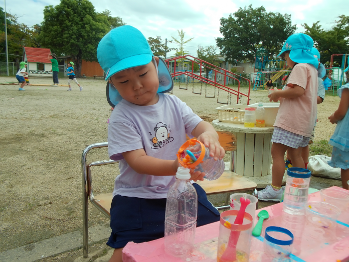 ペットボトルからペットボトルへ水の移し替えをしている3歳児