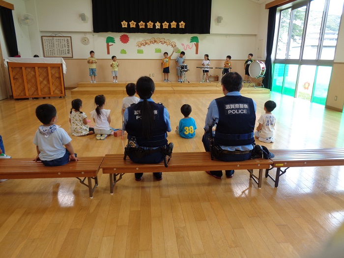 5歳児がお巡りさんを誘って音楽会で披露する合奏を聞いてもらっている様子