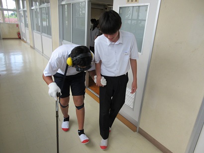 高齢者疑似体験グッズをつけて歩行する生徒と介助者として寄り添う生徒