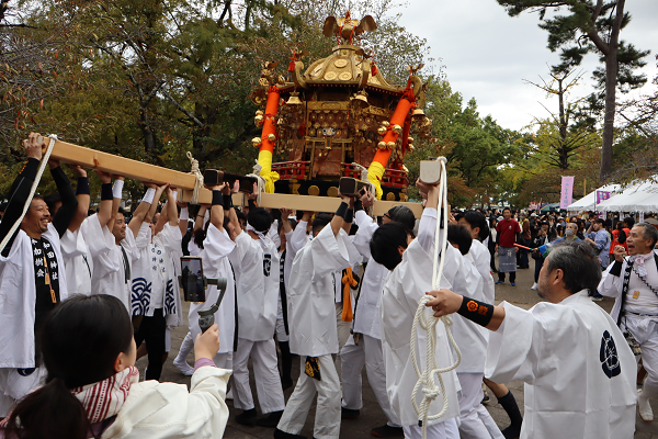 神輿巡行で、白い法被を着た人が神輿を担いでいる様子