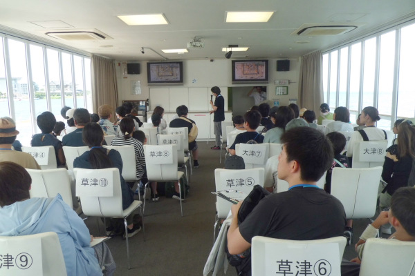 船の中で、景観についての話を聞く参加者の様子