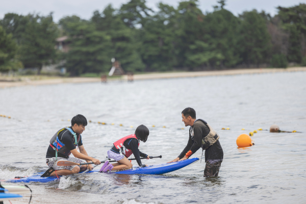 「松の浦水泳場」でSUPのボードに乗りこむ参加者親子の様子