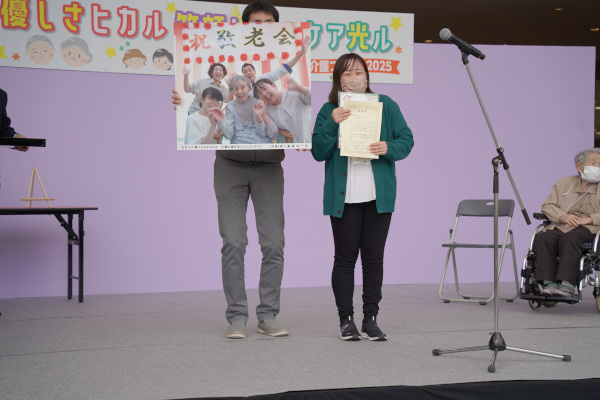 介護に関するフォトコンテストの大賞を受賞された方が賞状と受賞作品を掲げる様子