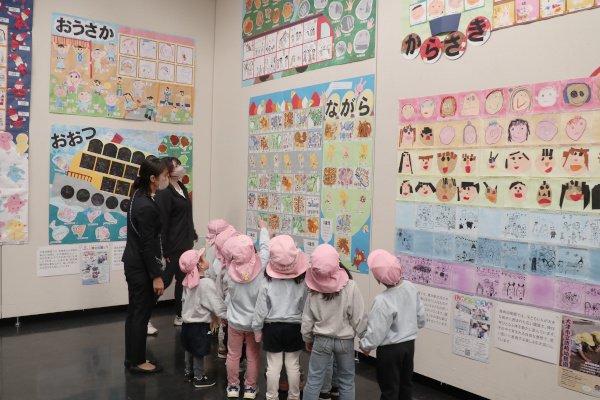 壁の作品を指さし鑑賞する市内園児と引率の先生の様子