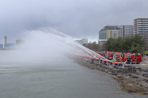 連なった消防車両から、びわ湖に向かって一斉に放水する様子