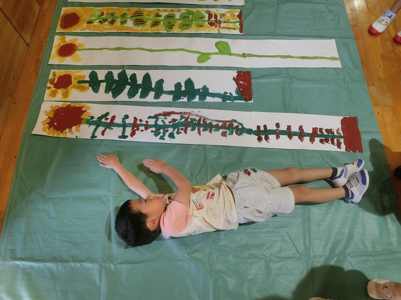 ひまわりの絵を描いた5歳児が背比べをしている様子