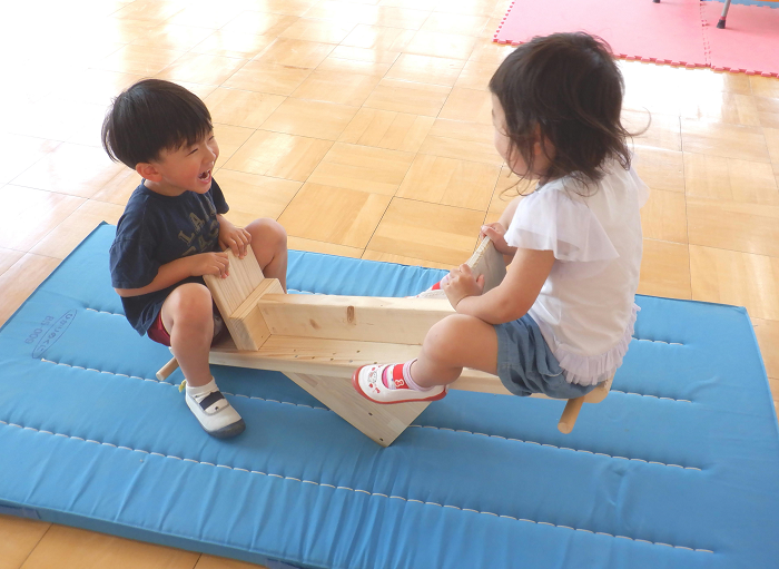 3歳児が木製の手作りシーソーで微笑み合いながら遊んでいる様子