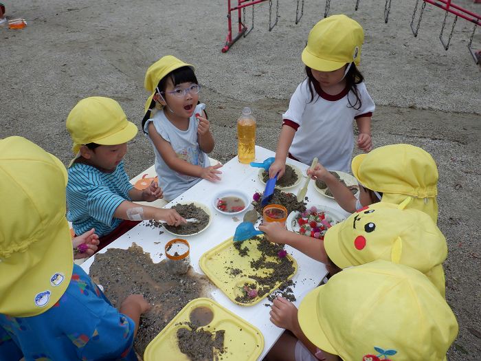3歳児が砂や草花でごちそうをつくり、みんなでパーティーをして遊んでいるところ