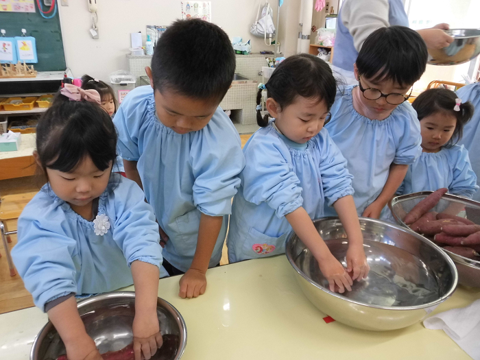 5歳児が3歳児にさつまいもの洗い方を教えているところ