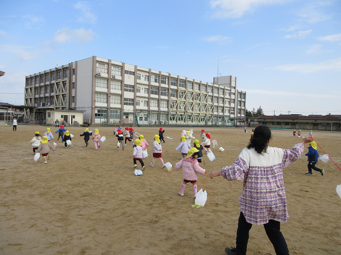子ども達が広い校庭で教師と一緒にたこあげを楽しんでいるところ。
