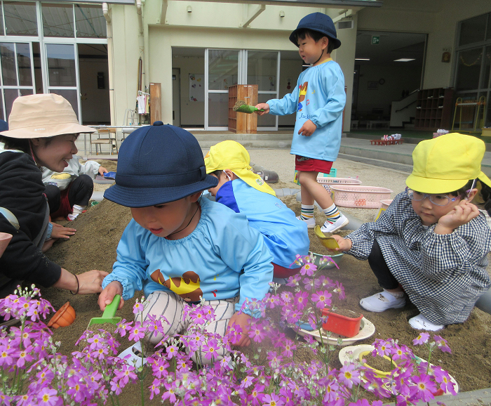 3歳児が先生や友達と砂場で遊んでいるところ