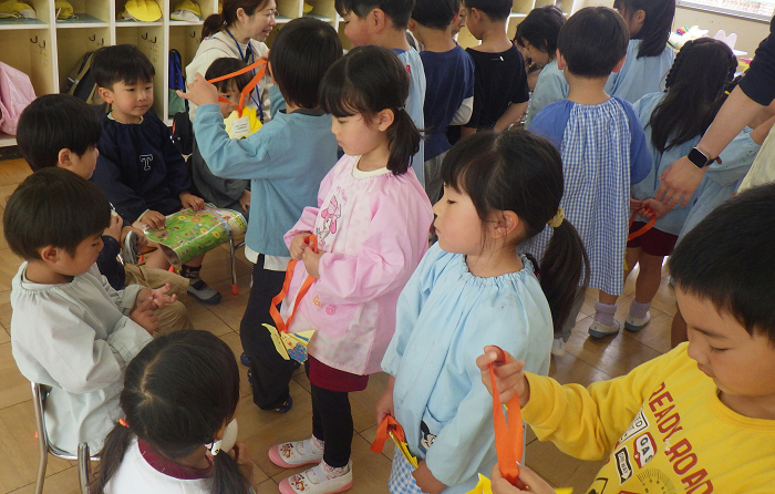 5歳児が3歳児に折り紙のペンダントを渡しているところ