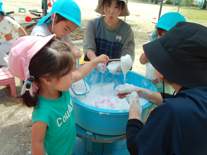 たらいにいっぱいの石鹸の泡で、3歳児が先生と遊んでいる