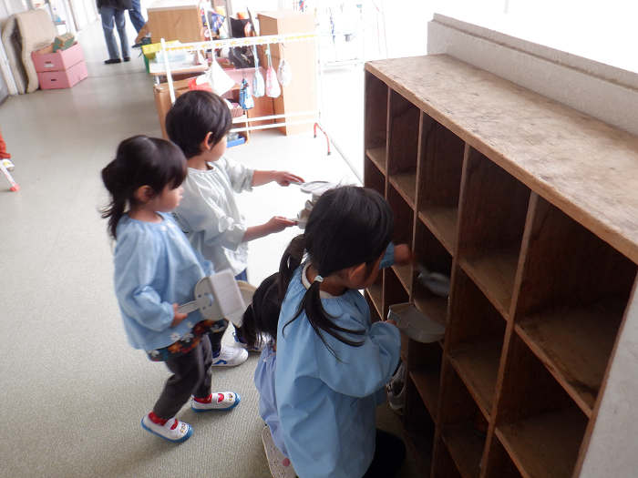 3歳児が小さなほうきで、下駄箱を掃き掃除している場面