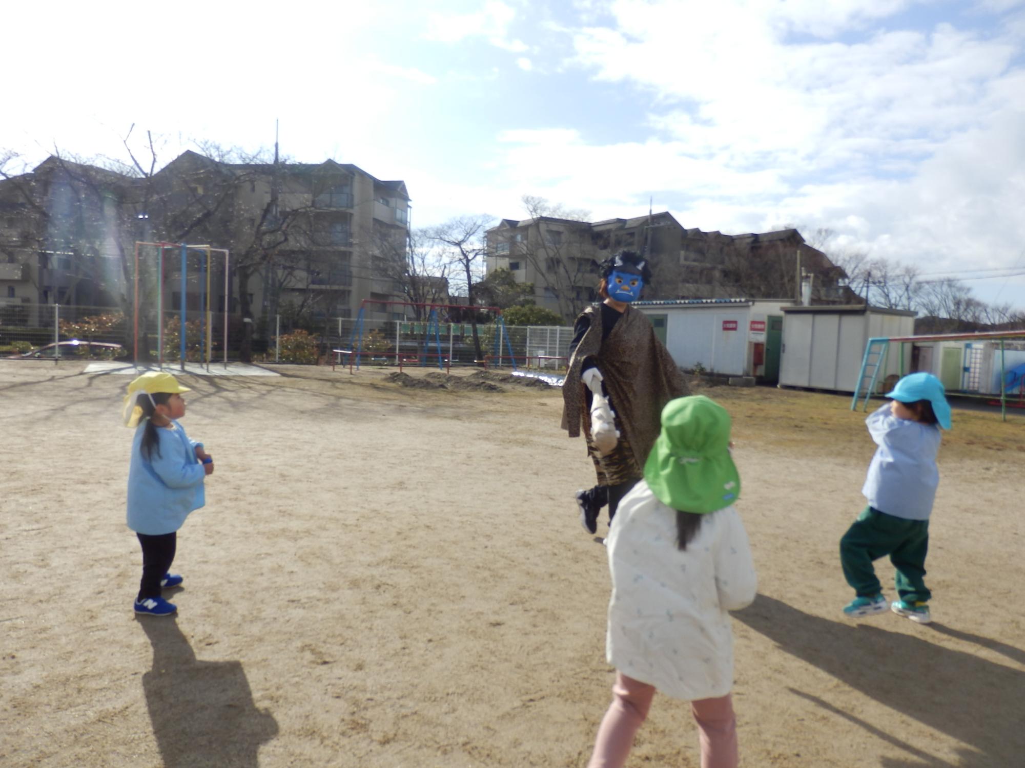 青鬼に扮した大人が三人の園児に囲まれ、豆を投げつけられている