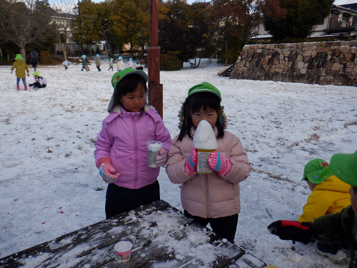雪をカップに入れてかき氷を作り、それを持っている4歳児