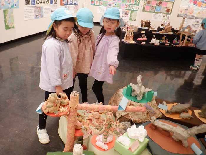 粘土で作った恐竜や雪だるまなどの作品を、友達と一緒に話しながら見ている様子