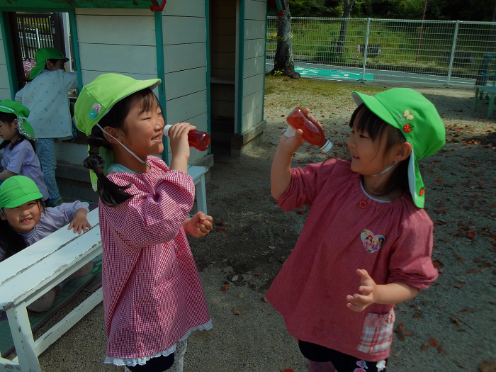 ペットボトルに入れたお花のジュースを飲む真似をしている二人の5歳児