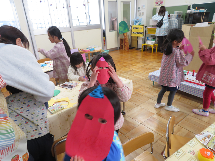 画用紙で鬼のお面をつくっている途中の子ども達。顔にお面を当てている様子