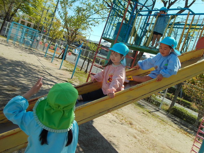 3歳児二人が滑り台を滑っていて、その様子を5歳児が見守っている