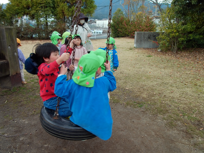 タイヤブランコに子ども3人が乗って揺れている