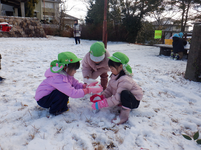 雪を集めて雪だるまを作っている三人の4歳児