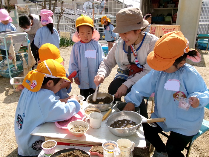 子どもと教師が砂と桜の花びらを使ってごちそうづくりをして遊んでいる様子