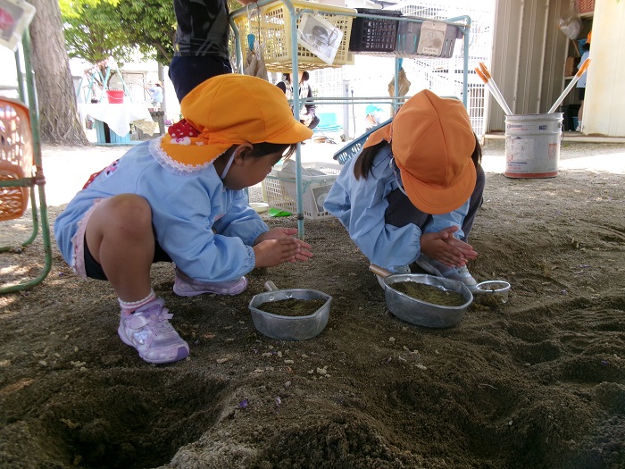 2人の子どもが友達と同じ方法でおなべに砂を集めている様子