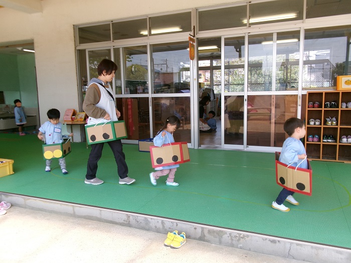子どもと教師が段ボールでつくった電車に乗って遊んでいる様子