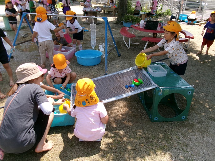 子どもと教師が波板でつくったすべりだいに手づくりの金魚を水の勢いで流している様子