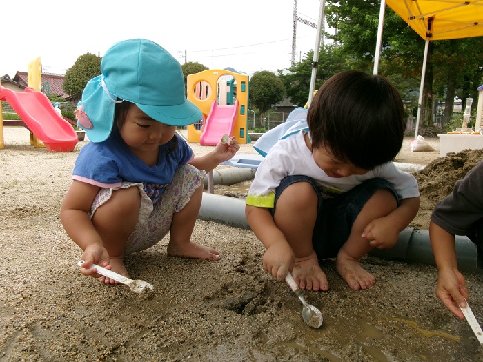2人の子どもがスプーンで地面の泥を叩いて、音が出ることを楽しんでいる様子