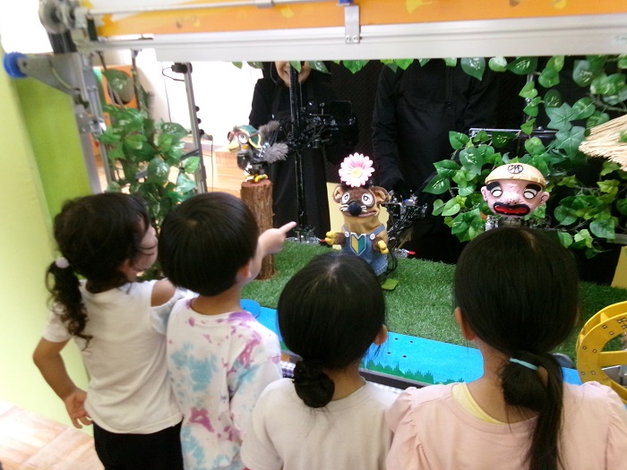 子どもたちが機械式人形劇の舞台を近くで見せてもらっている様子