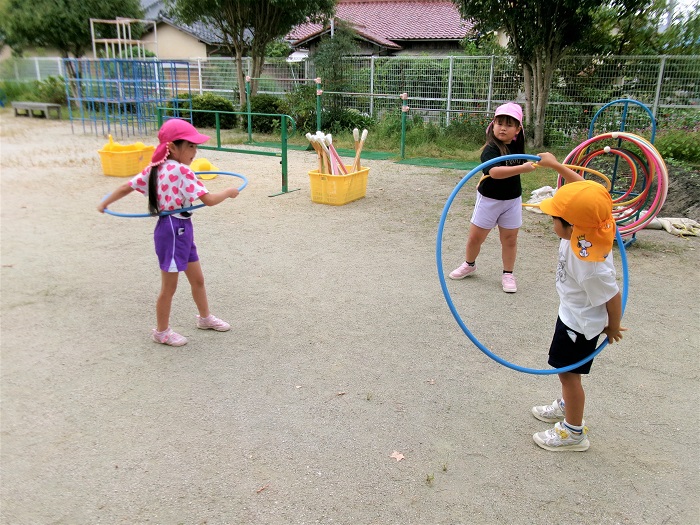 5歳児の子どもが4歳児にフープの回し方を教えてあげているところ