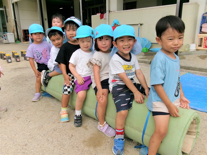 平均台にマットを巻いたものを電車に見立てて、子どもたちが乗って遊んでいるところ