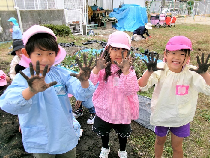 子どもたちが芋ほりで真っ黒になった手を見せている様子