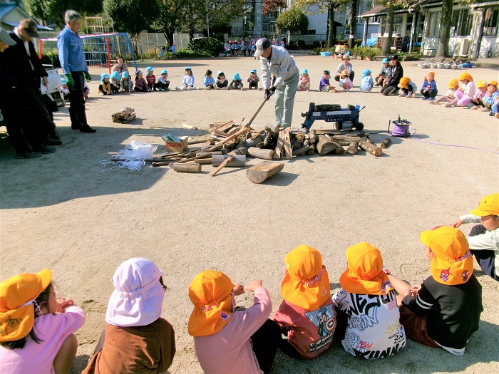 地域の方が薪割りをしてくださっているのを子どもたちが周りで見ている様子