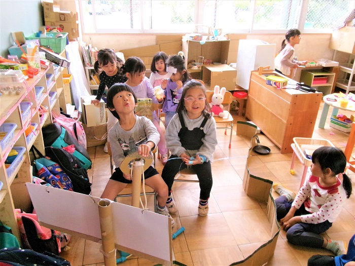 子どもたちが園児椅子を車の座席に見立てて乗り物に乗っておでかけごっこをしている様子