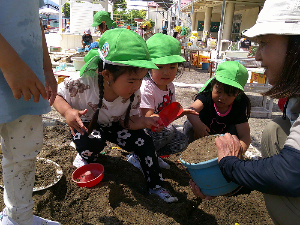 3歳児が砂場で先生と遊んでいる写真